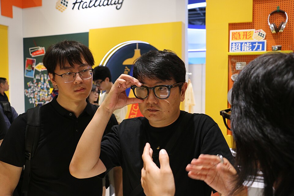 Young men checking out black rimmed clear glasses at what looks like a conference